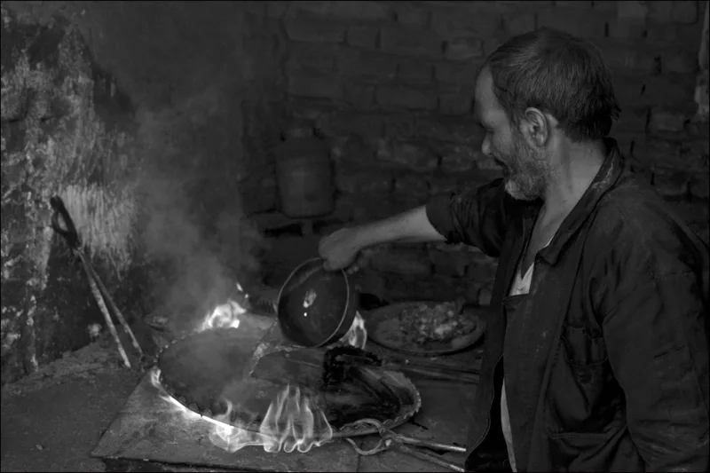 A man working beside a glowing fire in a dark workshop