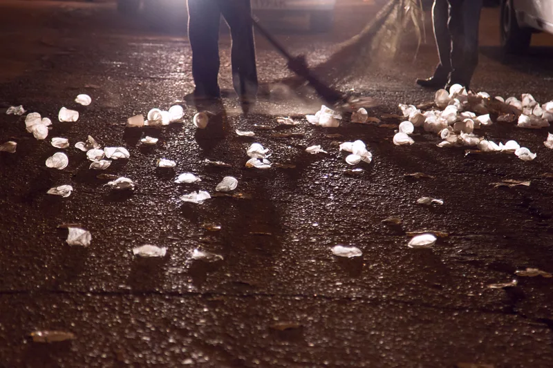 Figures standing in a pool of light on a street scattered with white objects