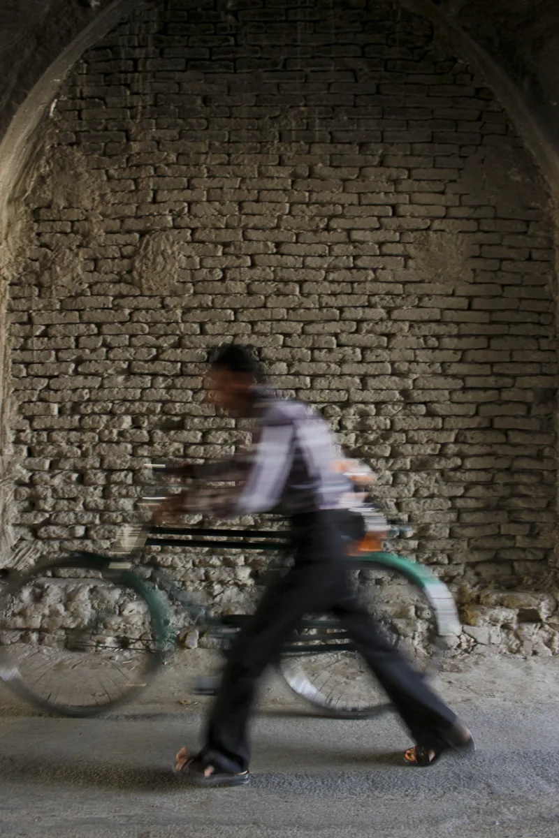 A blurred pedestrian walking past a brick wall and bicycle